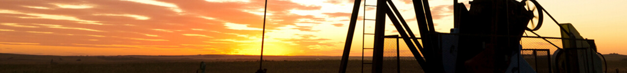 Pump jack in a field with the sun setting in the distance
