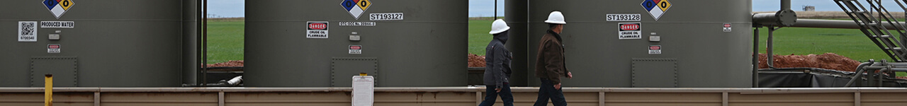 Two people in hard hats walking past large holding tanks
